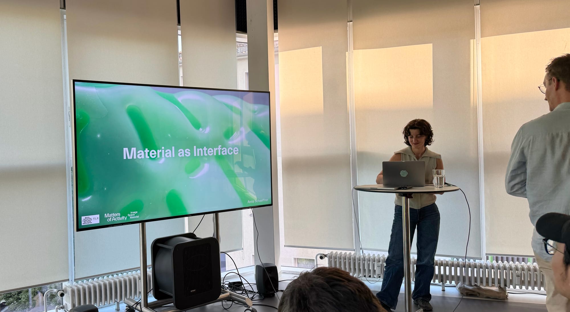 Photo of Anna Schaeffner at the start of her talk. The initial slide titled "Material as Interface" is visible on the screen