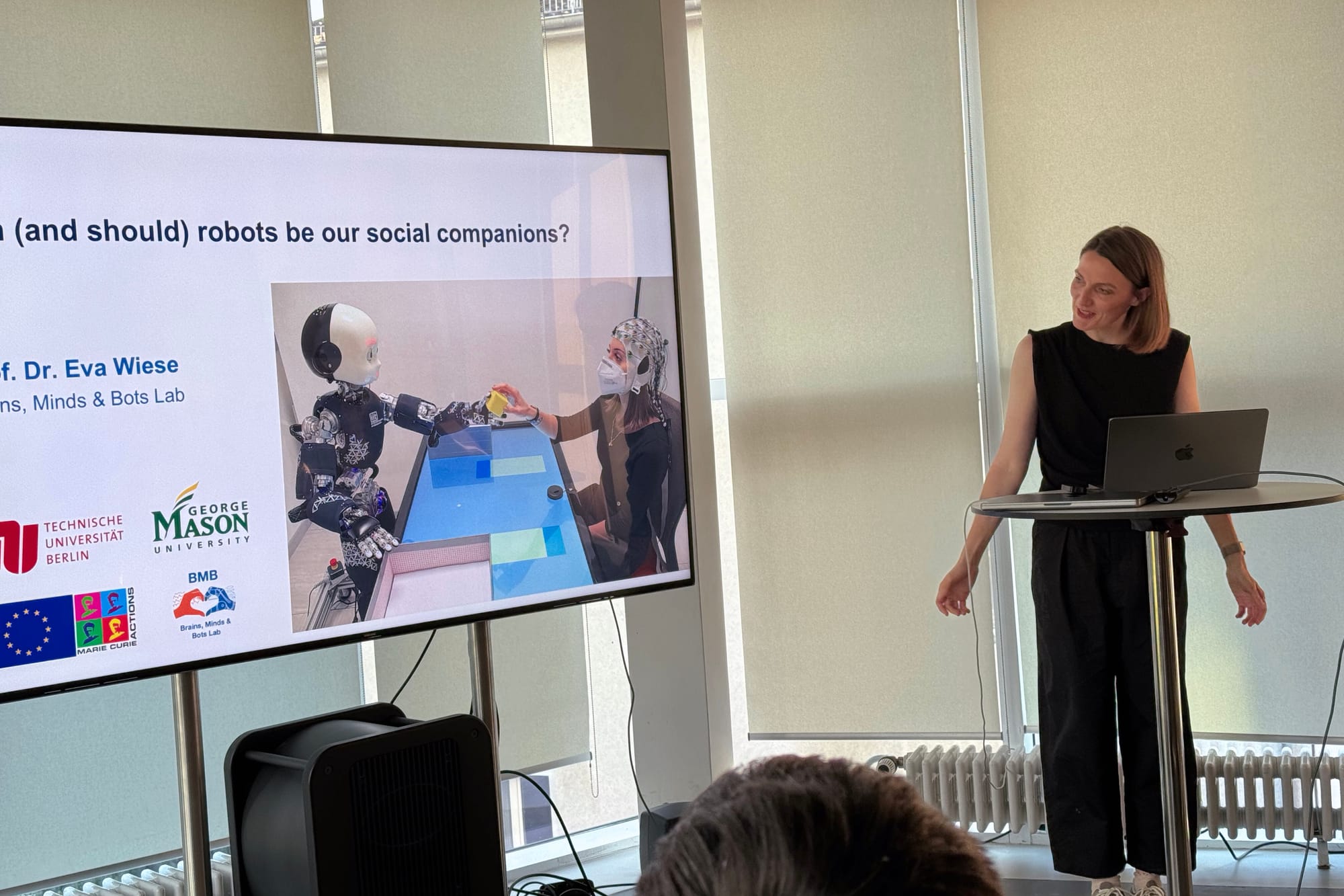 Photo of Eva Wiese at the start of her talk. The initial slide titled "Can (and should) robots be our social companions?" is visible on the screen